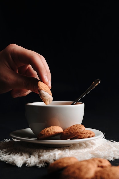 Unrecognizable hand dipping a cookie in hot coffee. Close up.