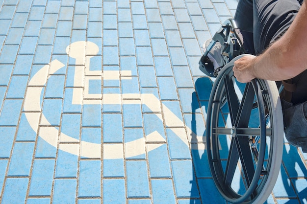 Unrecognizable handicapped man in a wheelchair passing over handicapped sign painted on the ground