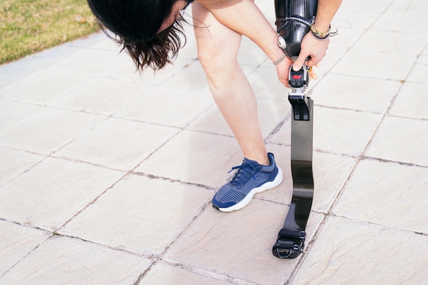 Unrecognizable male athlete bends to adjust the strap on his carbon fiber prosthetic leg