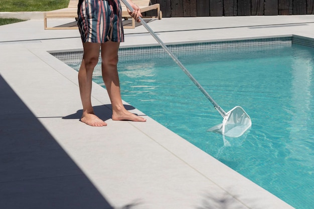 Unrecognizable man cleaning the swimming pool manually with white cleaning net at his house