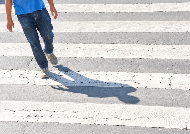 Unrecognizable man dressed in blue crossing the street at a crosswalk