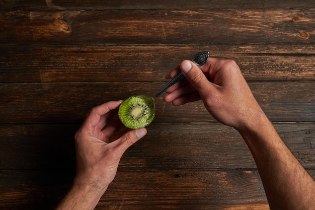 Unrecognizable man eating a kiwi with a spoonCopy spaceTop view