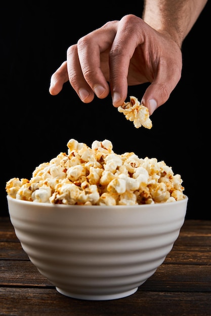 Unrecognizable man hand taking a delicious caramel popcorn from a white bowl on a black background