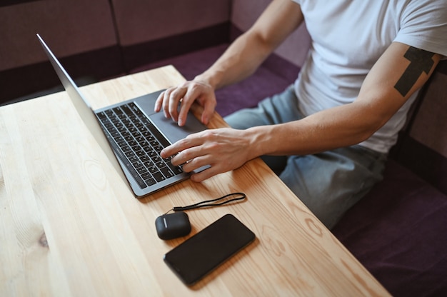 Unrecognizable man hands with smartphone and headphones working on a laptop