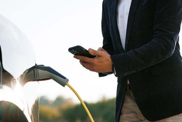 Unrecognizable man plugging electric car from charging station male plugging in power cord