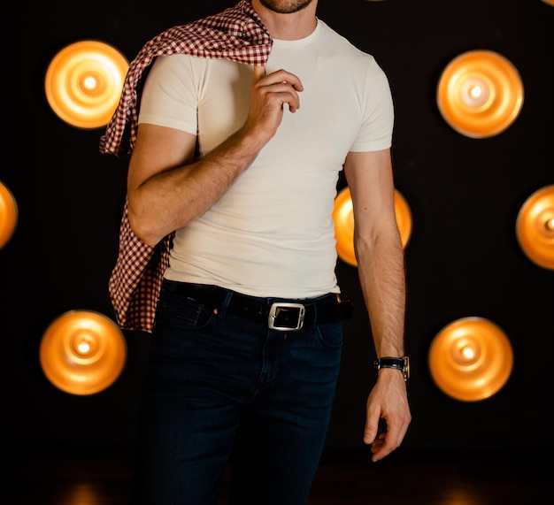 An unrecognizable man in a white Tshirt with a shirt stands in a dark room