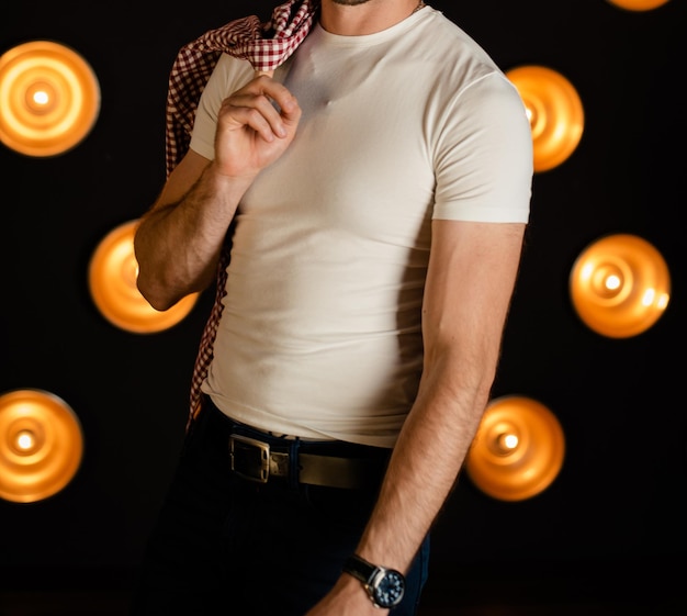 An unrecognizable man in a white Tshirt with a shirt stands in a dark room