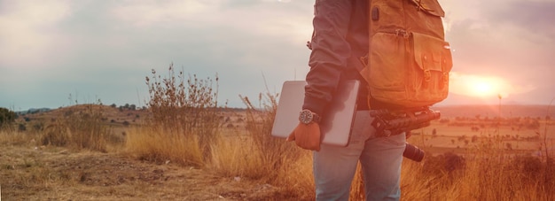 Unrecognizable man with a laptop walking at sunset