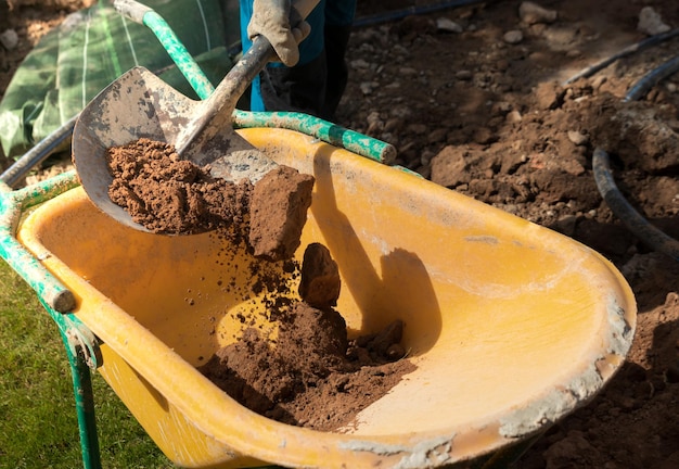 Unrecognizable man at work filling a yellow wheelbarrow with soil and stones