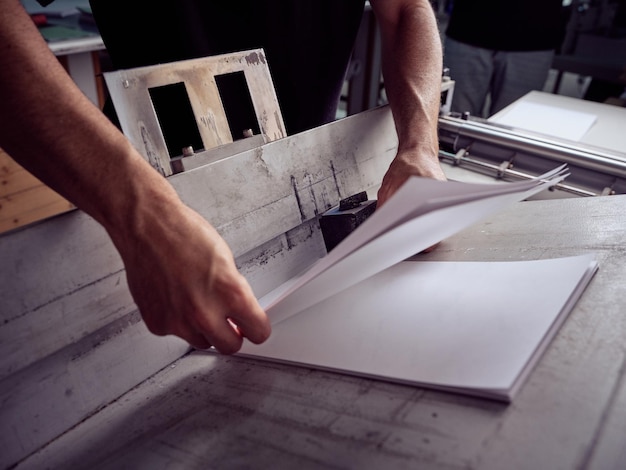 Unrecognizable man working with papers while standing at table and checking paper sheets in workshop