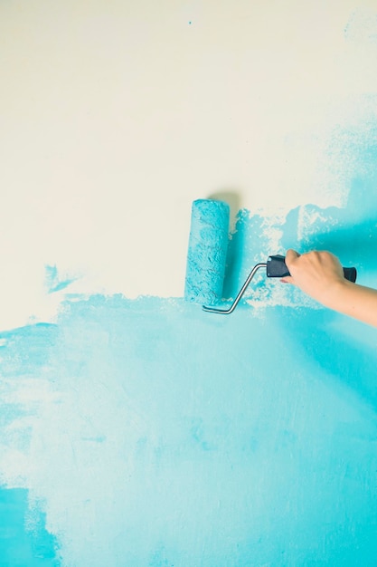 Unrecognizable person applying blue paint on wall Female hand with roller painting wall Concept of repair work and improvement of housing conditions