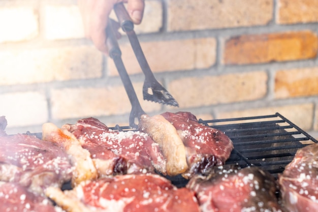 An unrecognizable person using a barbecue fork to poke one of the steaks being cooked on a grill