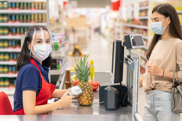 Unrecognizable supermarket cashier using computer to search for sauce price her customer going to buy