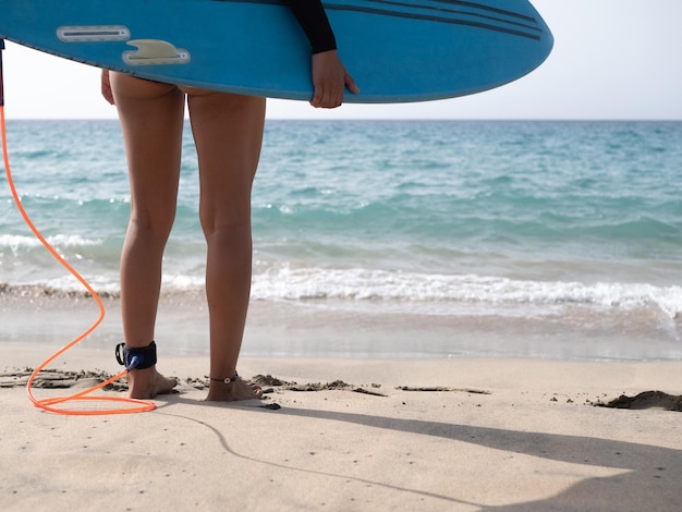 Unrecognizable surfer female standing on the beach shore