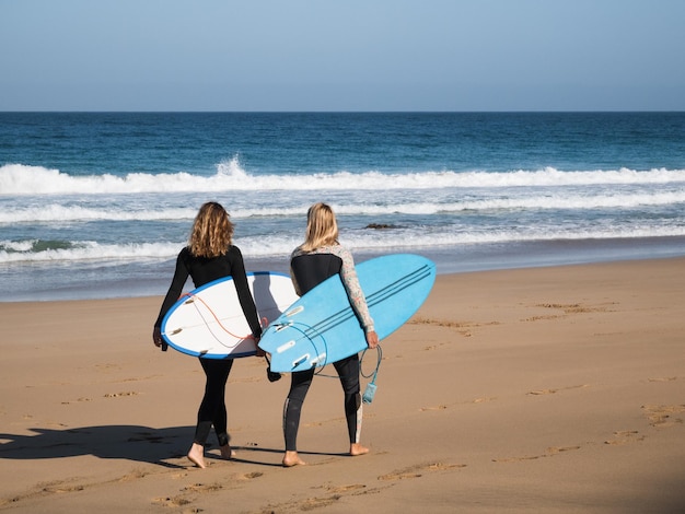 Unrecognizable surfer women walking by the beach shore