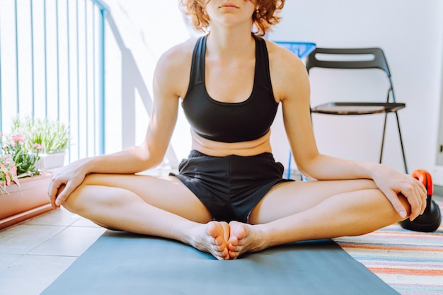 unrecognizable teenager in sports top and shorts sitting on gymnastic mat butterfly pose