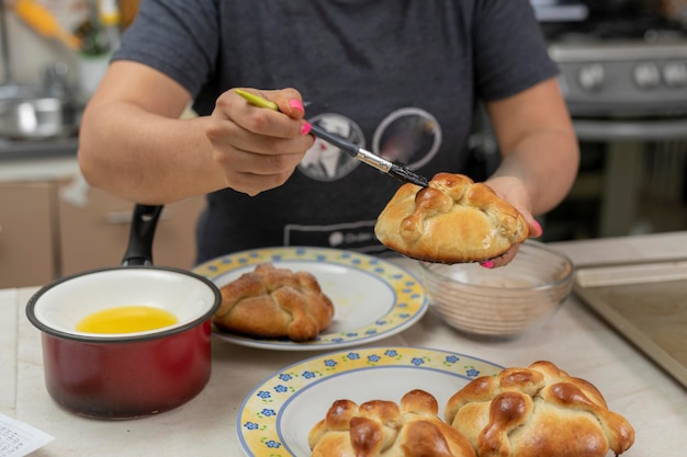 Unrecognizable woman buttering a pan de muerto she has just baked at home