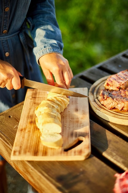 Unrecognizable woman cutting bread for bruschetta on wooden board