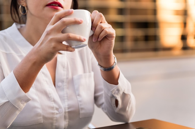 Unrecognizable woman drinking a cup of coffee on the terrace of a coffee shop, concept of urban lifestyle, copy space for text