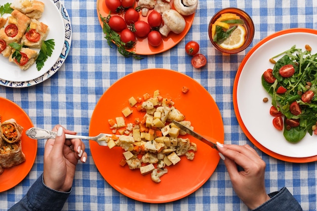 Unrecognizable woman eating fresh salad with greens and tomatoes on checkered tablecloth background. Healthy eating concept, organic vegetables top view.