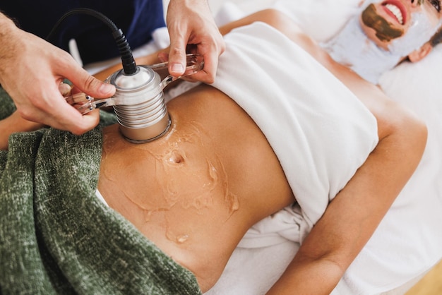 Unrecognizable woman getting an an ultrasound cavitation treatment to fat reduction on abdomen at the beauty salon.