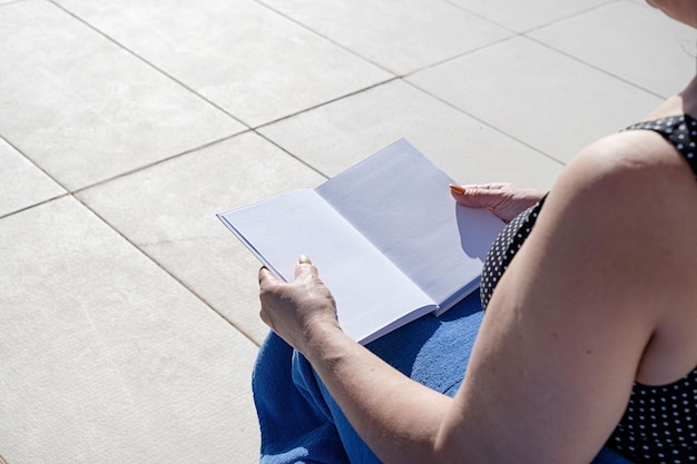 unrecognizable woman holding blank book for mockup design sitting by the swimming pool