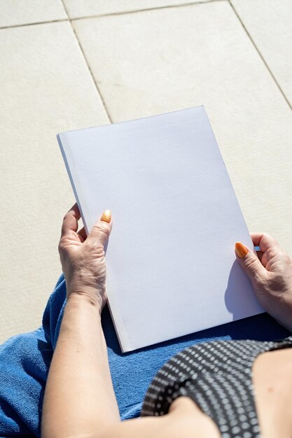 unrecognizable woman holding blank magazine for mockup design sitting by the swimming pool