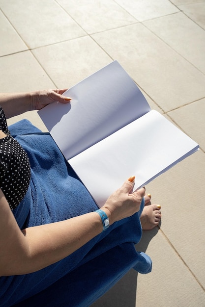 unrecognizable woman holding blank magazine for mockup design sitting by the swimming pool