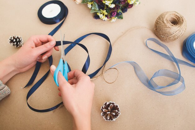 Unrecognizable woman make creative decorations from ribbons on beige surface