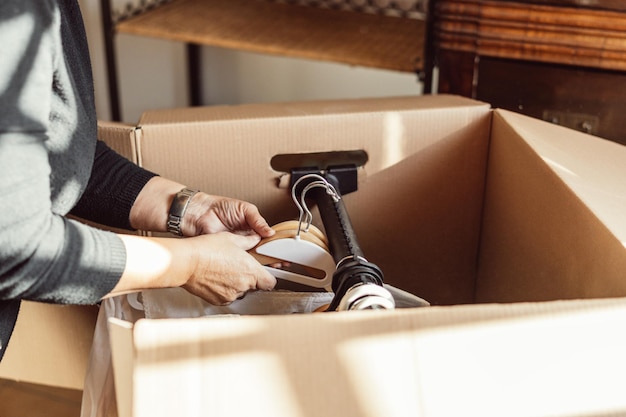 Unrecognizable woman putting clothes on hangers inside a cardboard moving box