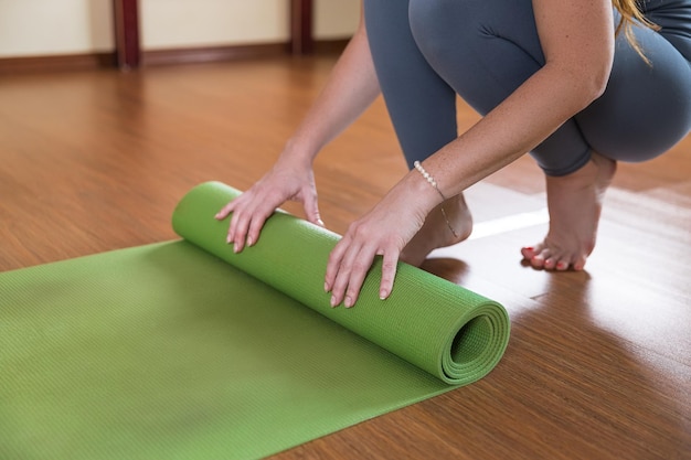 Unrecognizable woman roll up green mat for workout Slim girl in sportswear finish doing yoga fitness