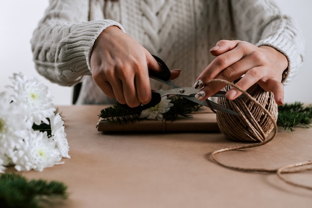 Unrecognizable woman with scissors cut natural rope for gift wrapping.