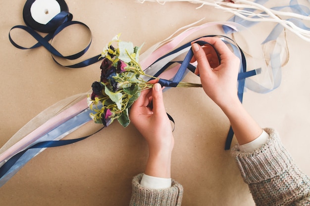 Photo unrecognizable woman wraps artificial flowers bouquet with blue ribbon