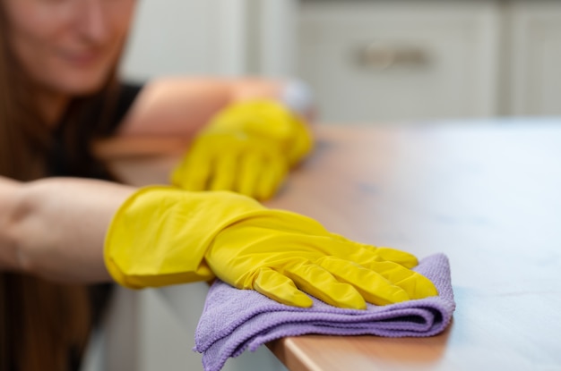 Unrecognizable woman in yellow gloves wiping wooden table top