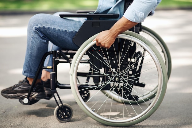 Unrecognizable young black man in wheelchair going for walk in city park closeup of legs