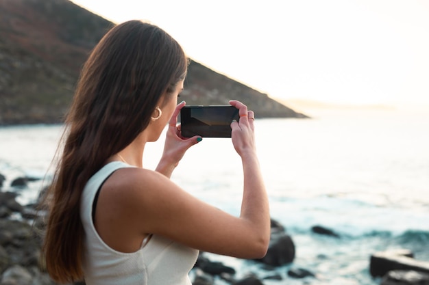 Unrecognizable young caucasian woman taking a picture of a beach and the sea with a smartphone