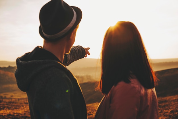 Unrecognizable young couple looking at majestic sundown sky while standing in countryside field together.Young couple admiring sunset