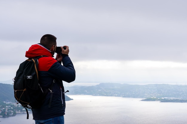 Unrecognizable young man with his backpack on his back and photographing the city of Bergen and the fjord in Norway