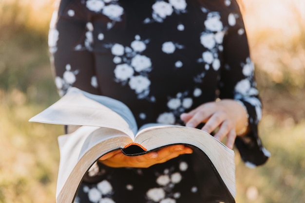 Unrecognizable young woman holding and reading her bible, outside with sun backlight. Protestantism