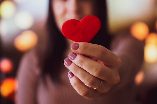 Unrecognizable young woman holding a small red heart with one hand