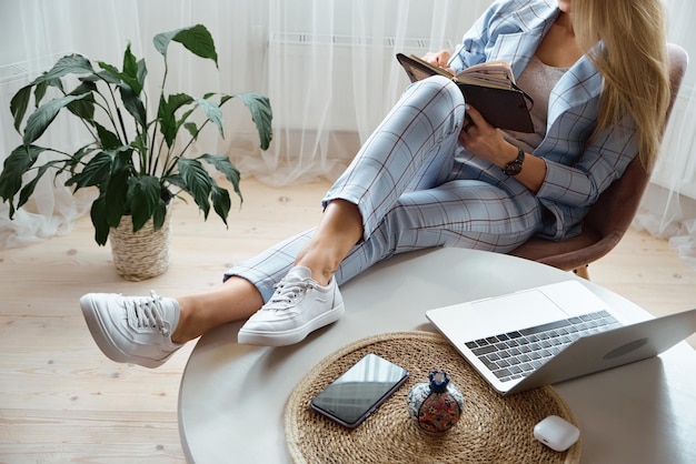 Unrecognizable young woman making notes in notebook sitting at workplace at home remote work