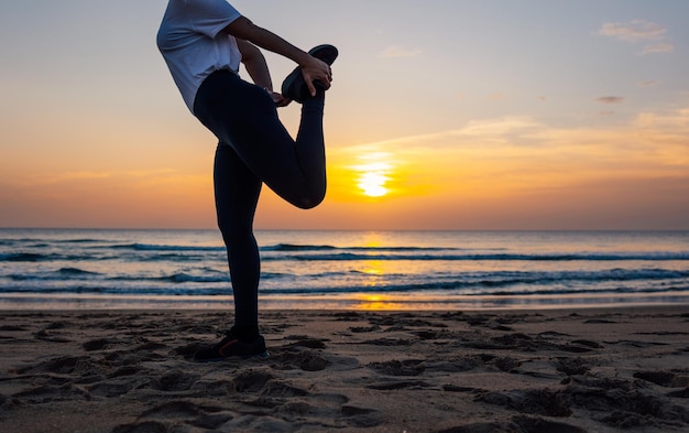 Unrecognizable young woman stretching before training on the beach at sunset