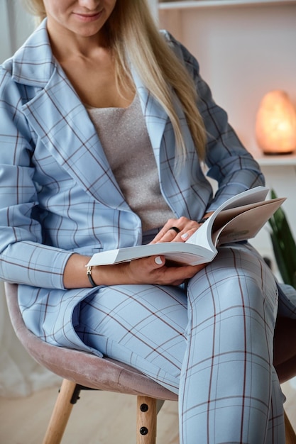 Unrecognizable young woman in a suit reading a book sitting on a chair