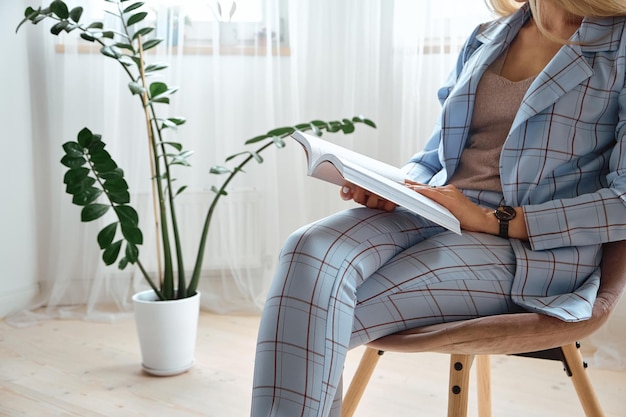 Unrecognizable young woman in a suit reading a book sitting on a chair