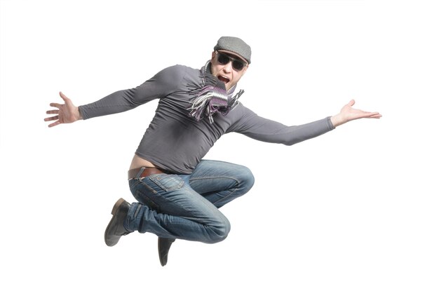 Unshaven bald man wearing a cap jeans sunglasses and scarf jumping Isolated