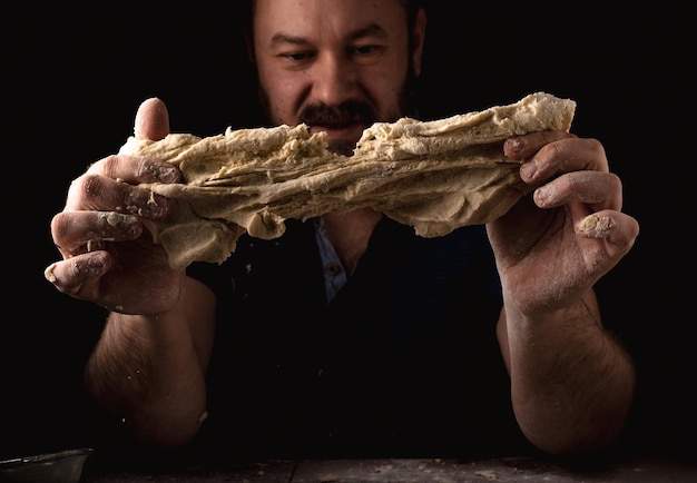 Unshaven man kneading dough on a black background