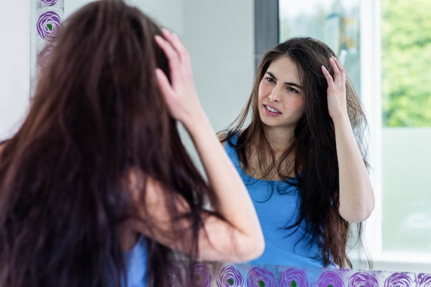 Unsmiling brunette looking her reflection in the mirror in bathroom