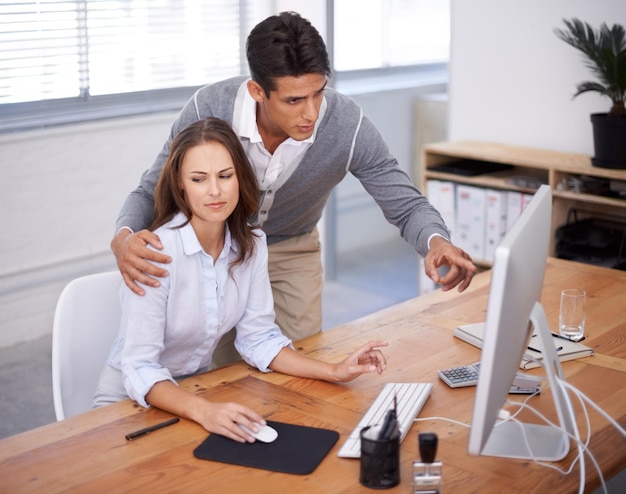 Unsuitable behaviour for the office A young woman looking uncomfortable as her boss puts his hand on her shoulder