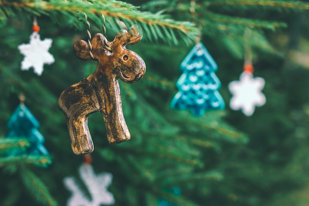 Unusual ceramic toys in the shape of an elk, a Christmas tree and snowflakes hang on a spruce branch. Decorations for the new year, festive mood