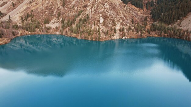 Unusual mirror color of water in a mountain lake. It reflects trees, mountains and the sky.